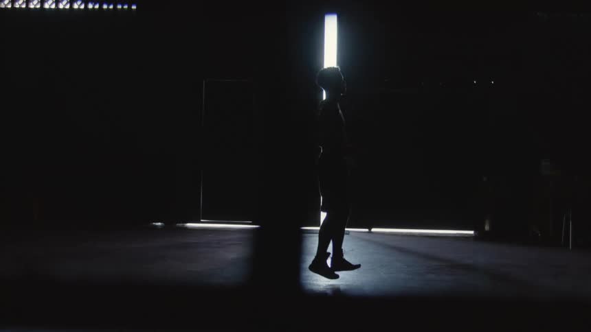 A man is jumping rope inside a dark building with large bay doors during the daytime