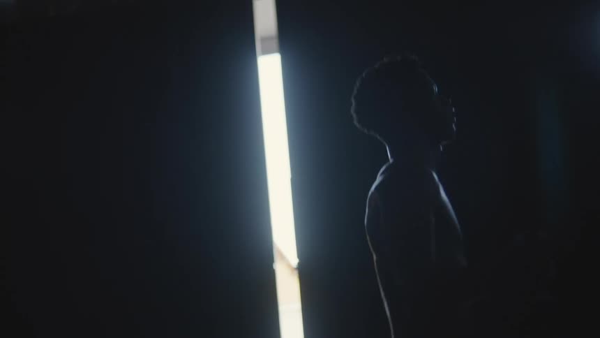A man is jumping rope in a room that is almost all black