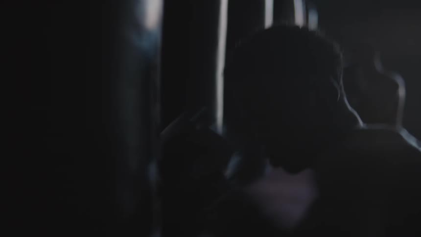 A man wearing boxing gloves is hitting a punching bag repeatedly as another man does the same in the background