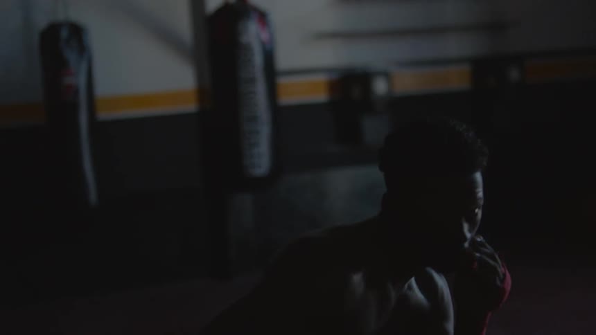 A dark gym where two males are air boxing