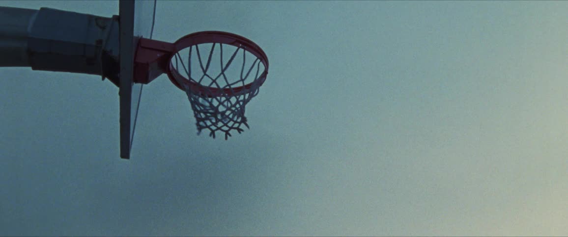 A young man is playing basketball in the day time