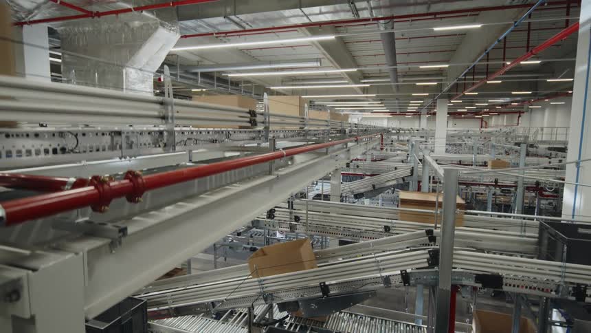A drone shot of the production line inside a sprawling warehouse or distribution center, showcasing a seamless flow of bins and boxes as they traverse through a highly automated factory