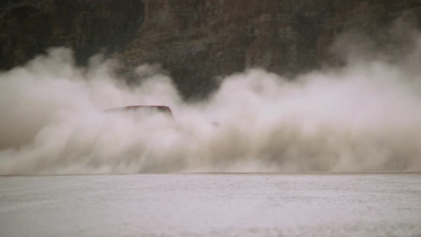 A red pickup truck is spinning out and smoking near mountains
