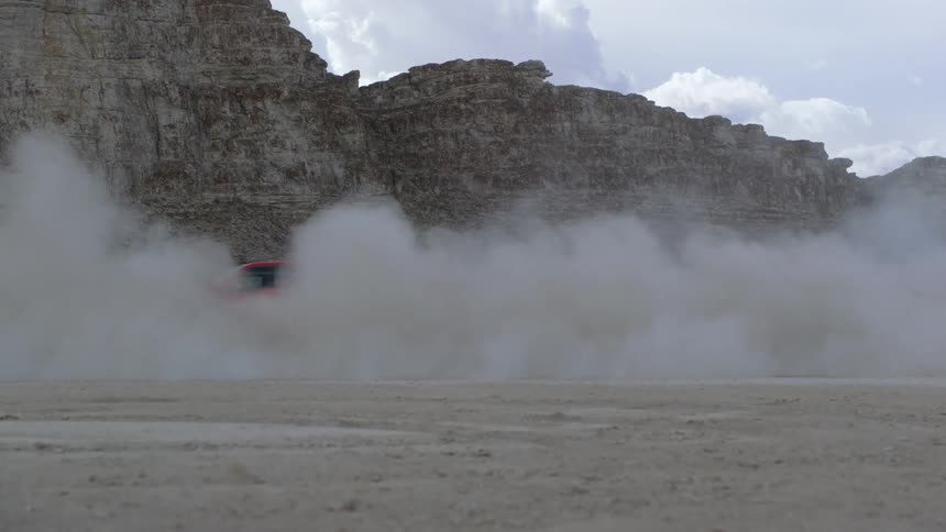 A red pickup truck is spinning out and smoking near rock formations in the desert badlands
