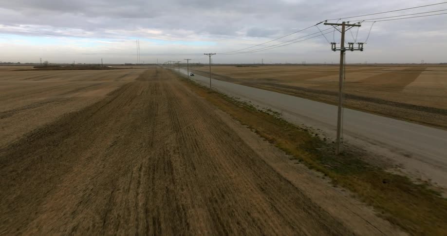 A vehicle travel along a road through a rural countryside on a cloudy day