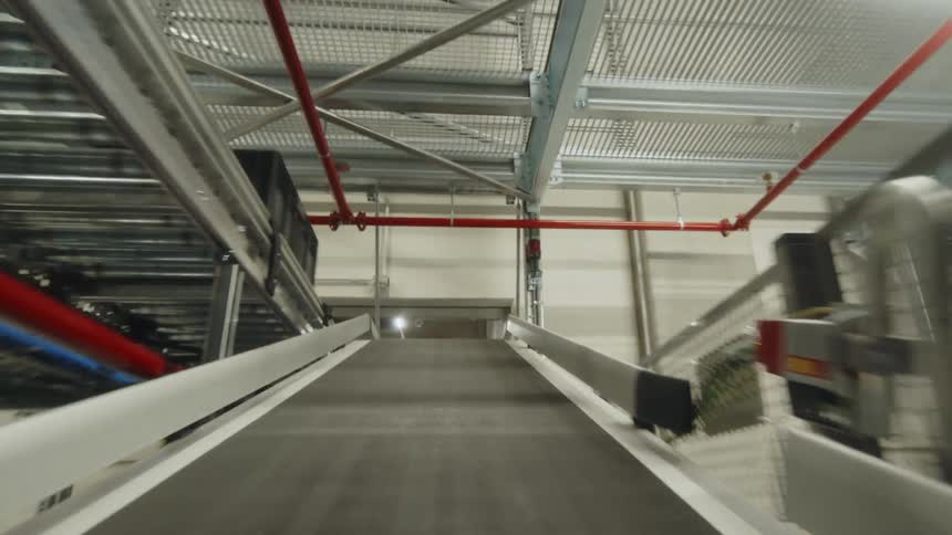 A first-person POV shot of a box moving along the tracks of a shipping warehouse or distribution center