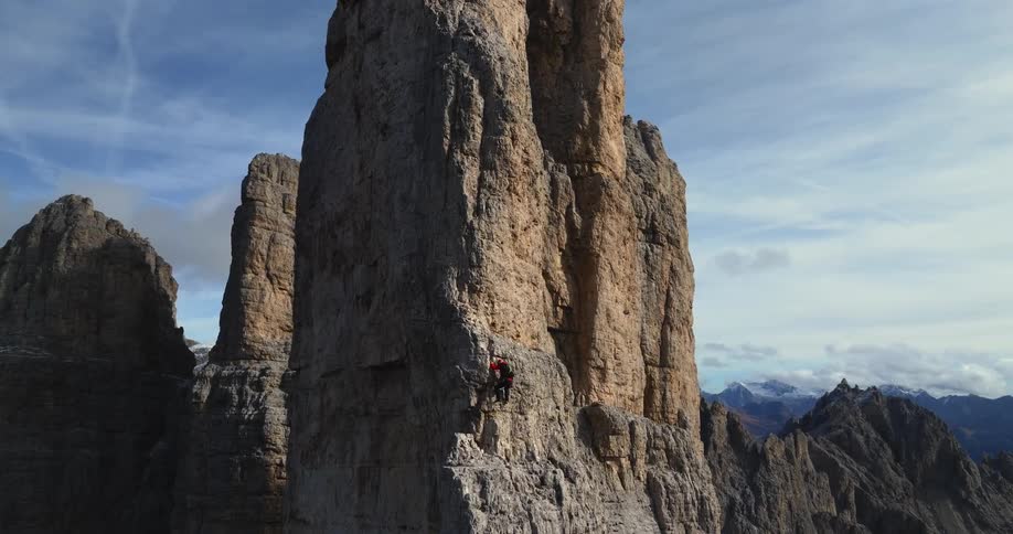 A person is climbing up the side of a huge rock formation in the badlands under a cloudy sky