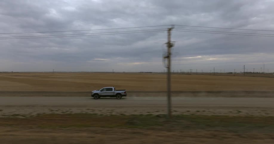 A vehicle is driving down a road in a rural area at dusk