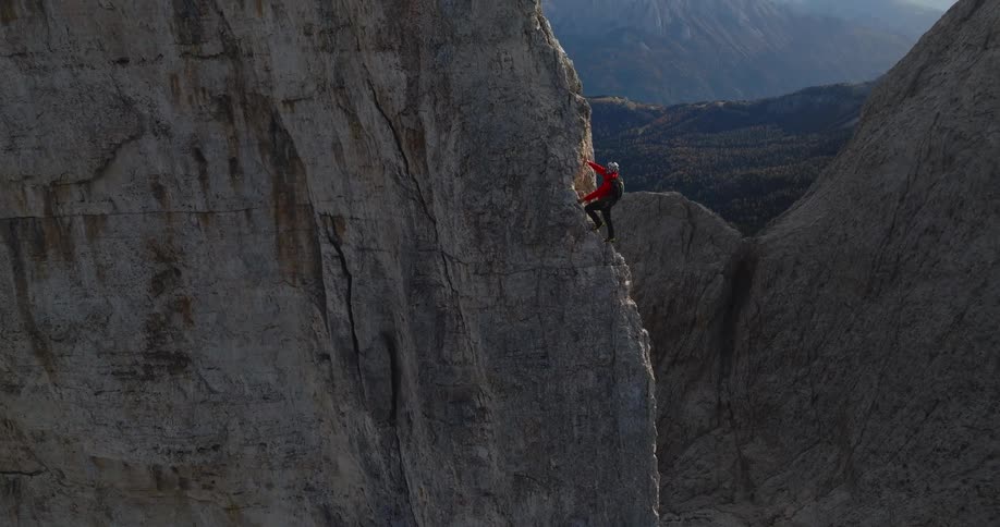 A rock climber ascends a natural rock face high up in a mountain range during the day