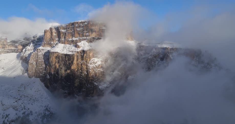 An aerial view of snowy mountains with clouds rolling over them