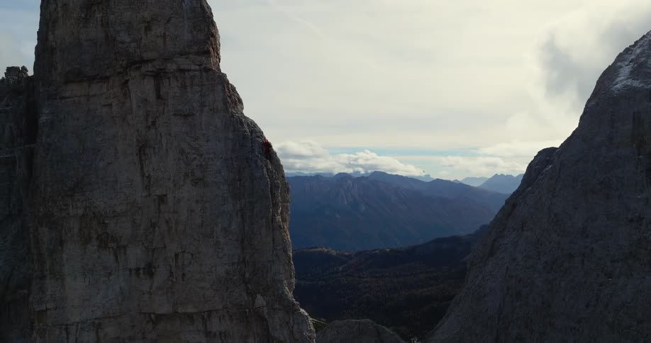 An aerial view of mountains and a man climbing a rocky ridge during the day