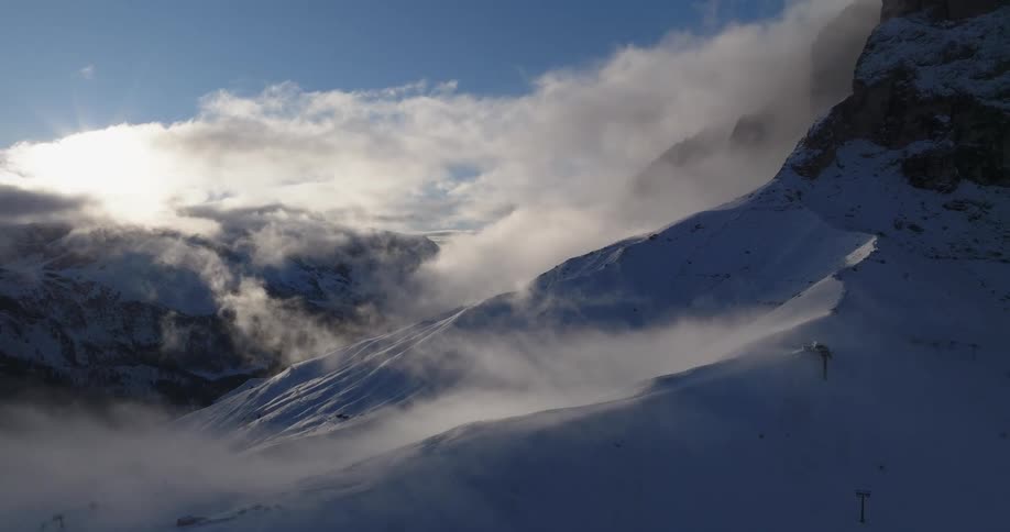 Aerial view of clouds hanging over the snow covered slopes of a mountain range at evening