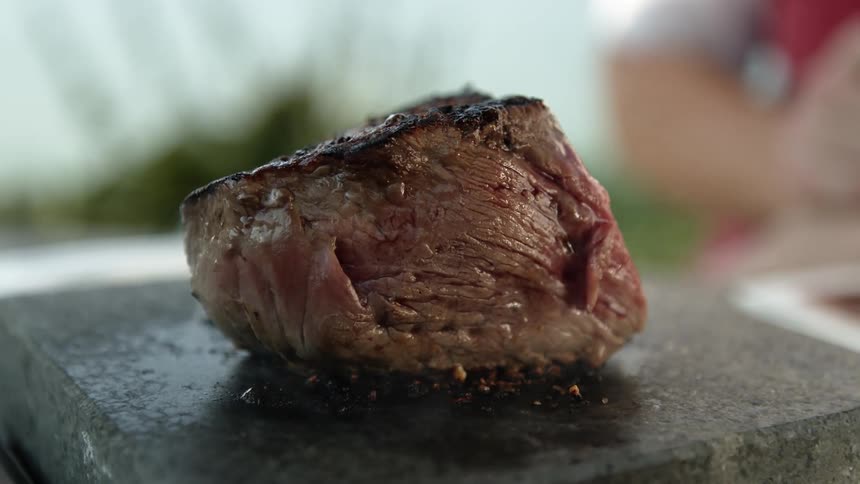 A piece of steak is cooking outdoors on a stove