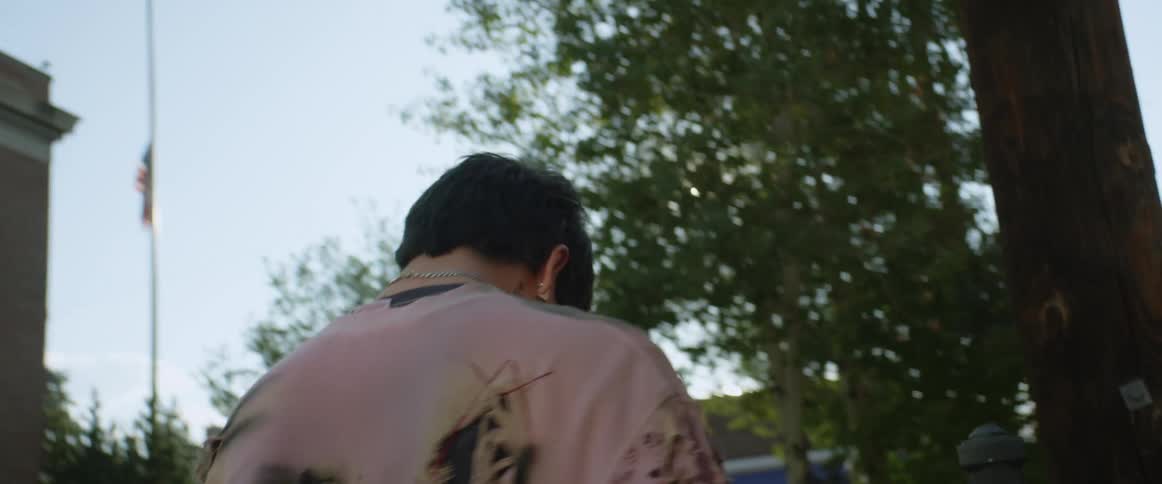A teenage boy is standing outside of a school nodding his head and turning around