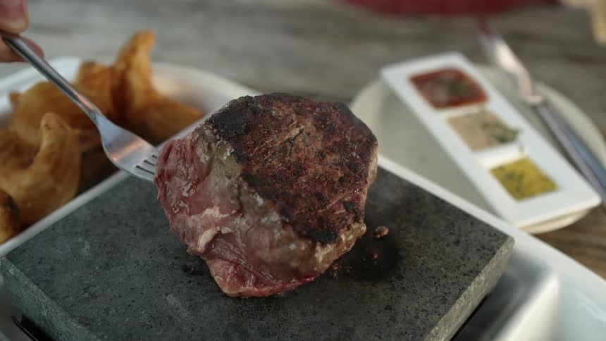 A fork penetrates a steak cooking on a grill and flips it over very slowly