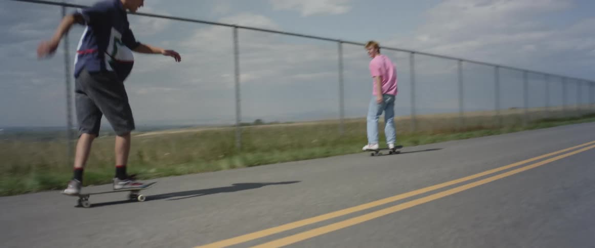 A group of boys skateboarding on the road along a fence