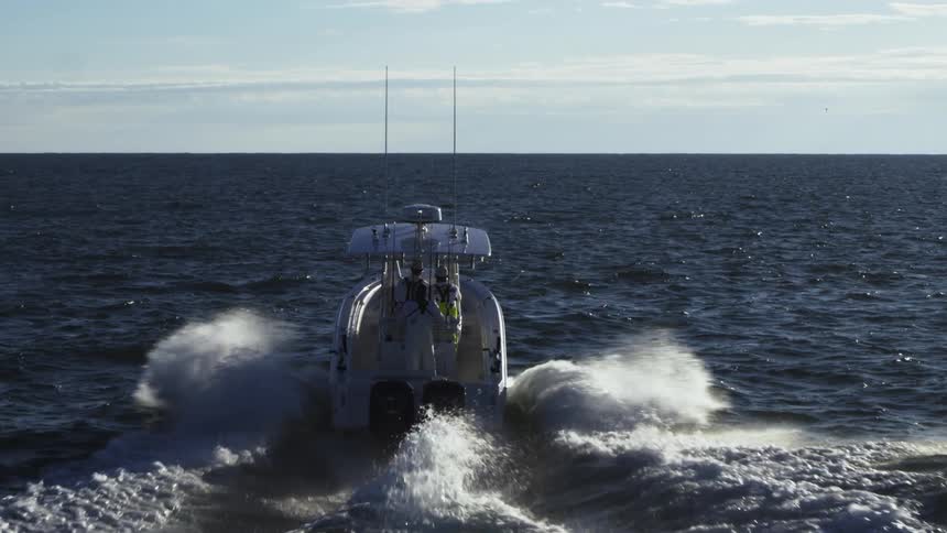 People stand on a speedboat as it makes waves through the ocean