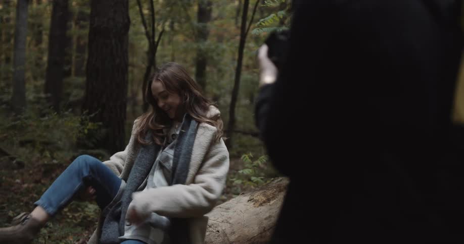 Young attractive woman sitting on a fallen tree in the forest modeling for a photographer