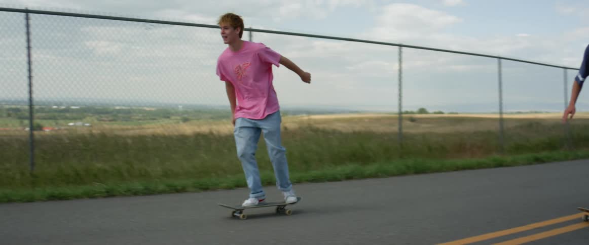 A group of young men run and jump onto their skateboards together before skating down a road