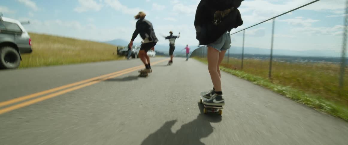 A small group of teens are shown from behind skateboarding down a concrete road