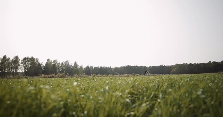 A wide open view of a grass field with two people running and chasing each other in the distance