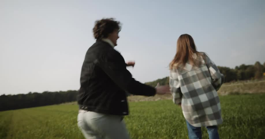 Couple run and play in field bordered by trees