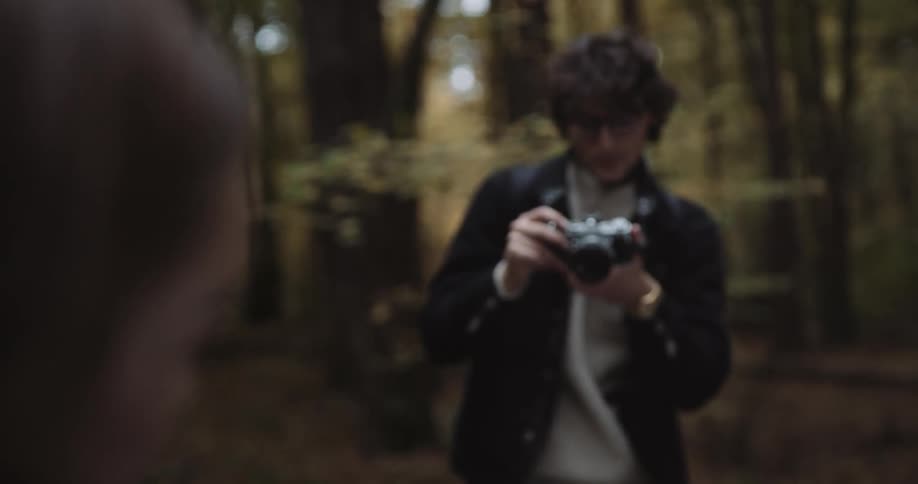 Woman poses as she and male photographer stand in woods among fallen leaves