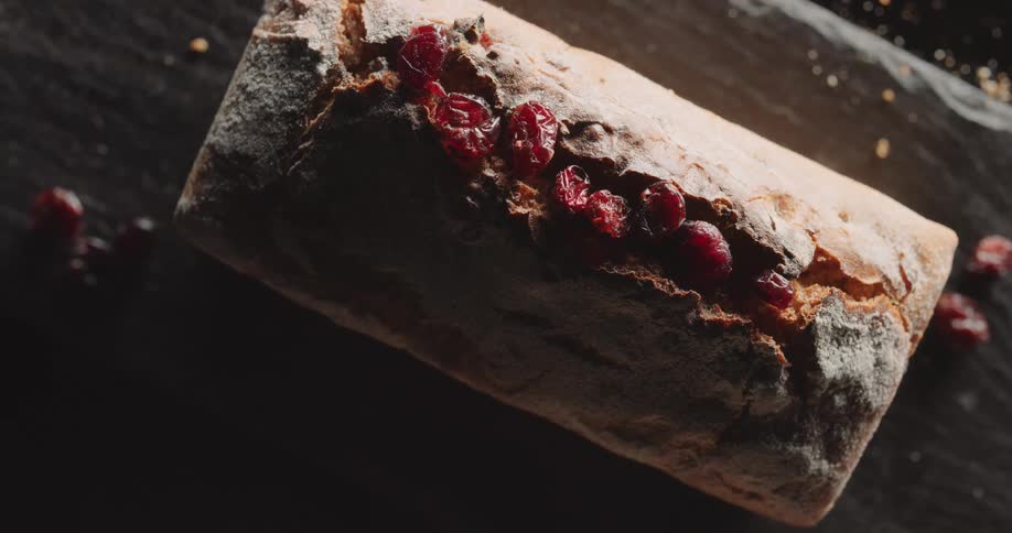 Fruit topped bread loaf sits on rough wooden board