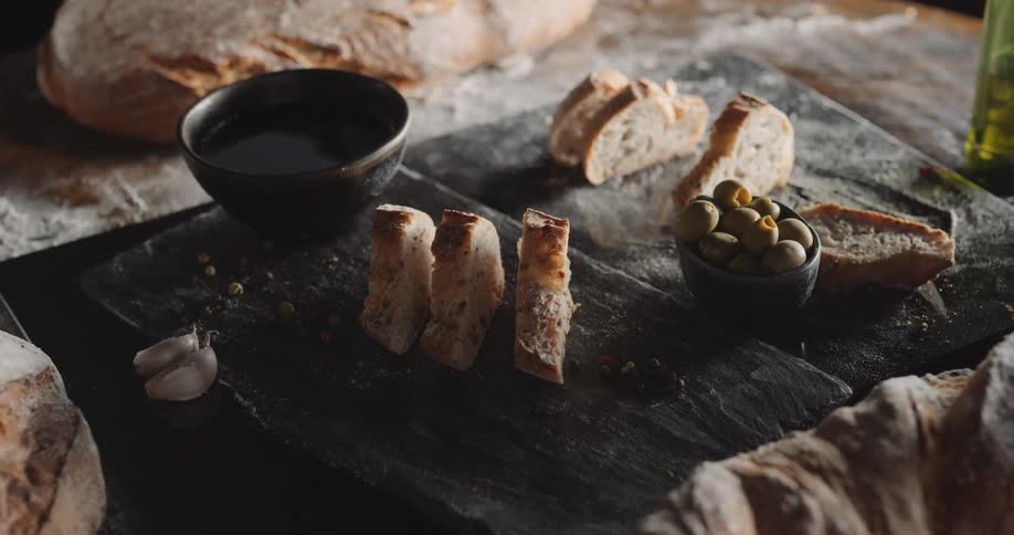 Slices of bread and a bowl of olives are displayed on a stone platter