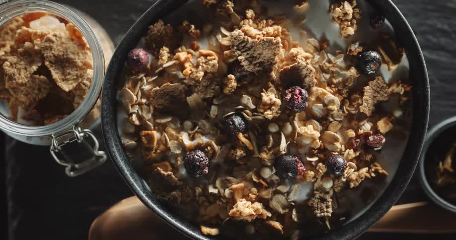 A top down view of a bowl of bran flakes with oats and berries sitting on a wooden table in a kitchen