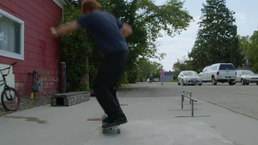 A teenage boy is riding a skateboard on a neighborhood sidewalk and leaps on a rail and rides across it before landing back on the sidewalk