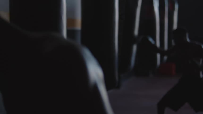 Two men practice with punching bag in dim gym
