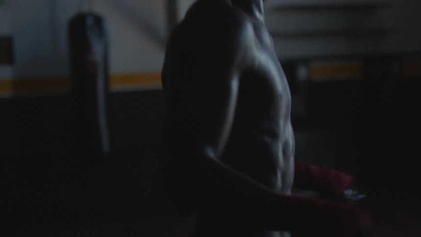 Muscular shirtless man rope jumping on a dimly lit gym