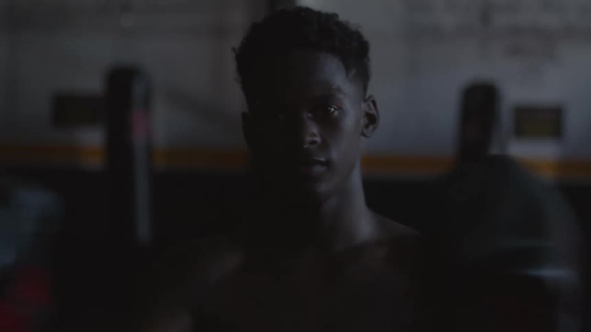 A male is standing in a gym and wearing boxing gloves