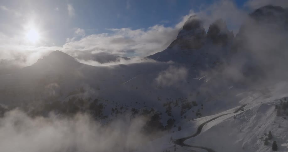 Fog rises from a snow covered mountain valley as the sun shines brightly through the clouds