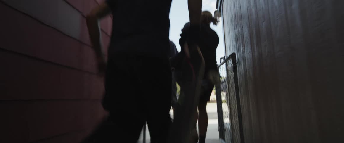 A group of men carrying skateboards runs down alley and gets on skateboards