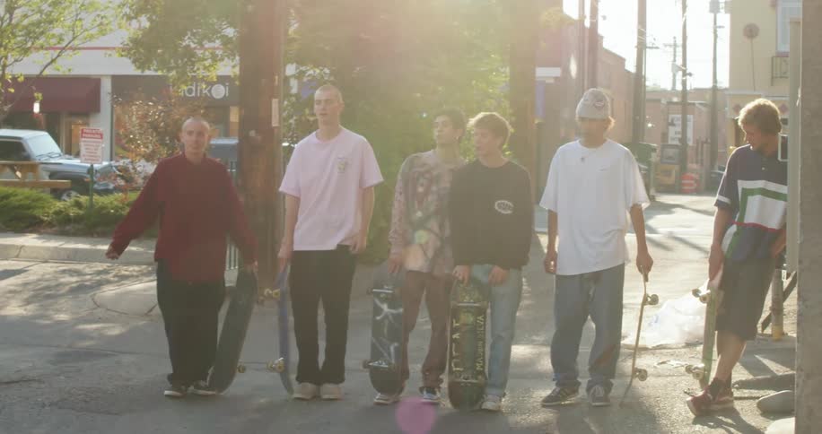 A group of boys with skateboards stand in a row in an alley