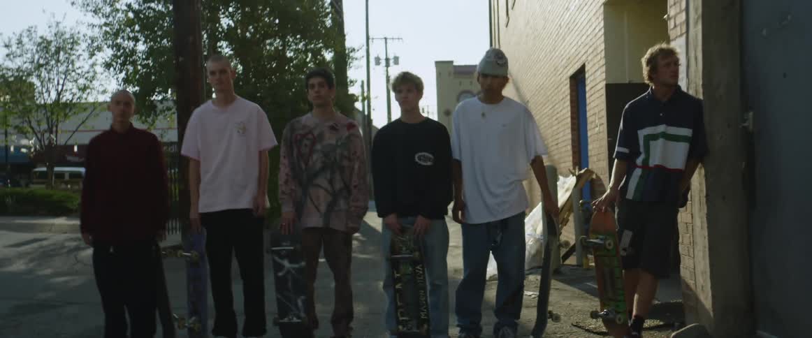 A group of men pose in an alley with their skateboards