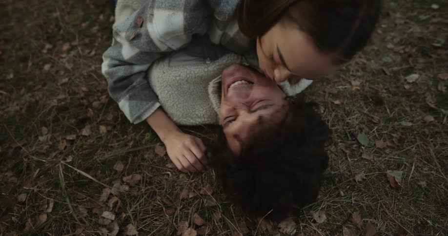 Man lying on the ground outdoors while his girlfriend is hugging him and kissing his face