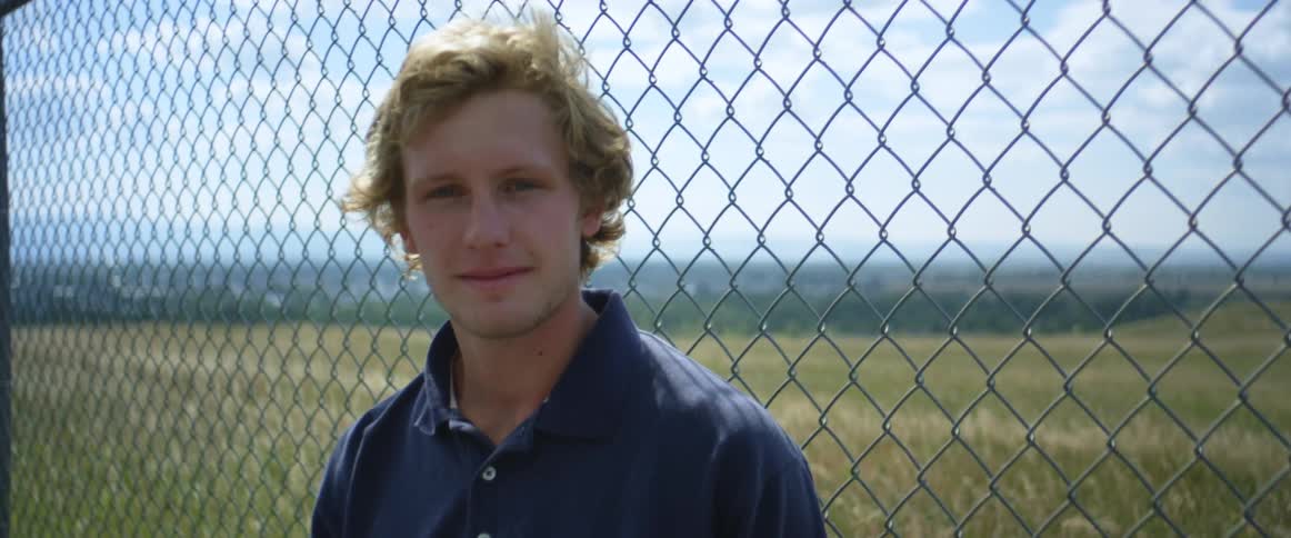 A male is standing outdoors next to a fence during spring