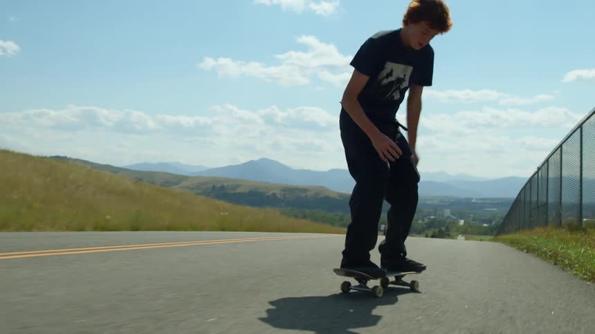 A teen is skateboarding outdoors on an empty road