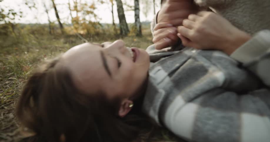 Young couple lying on the ground in a grass field hugging each other tickling each other and having fun together