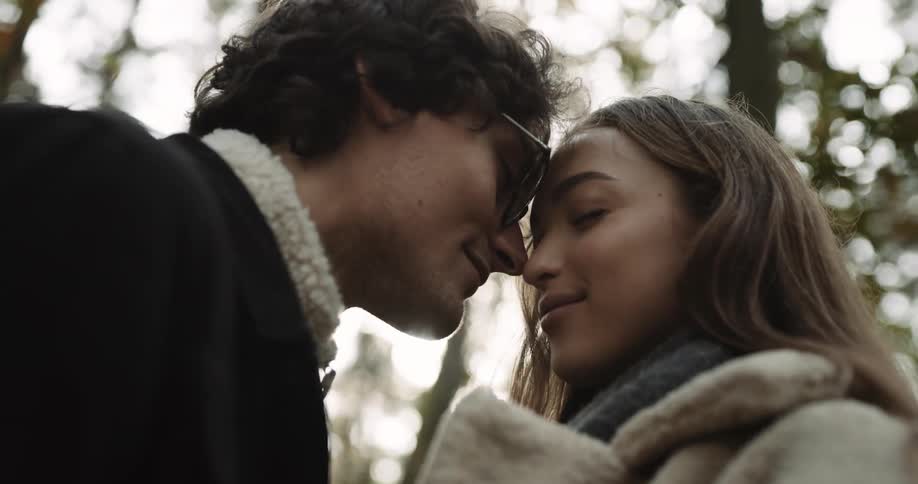A woman and a man nuzzle noses and smile at each other before almost kissing