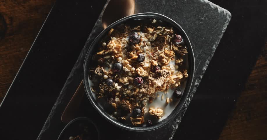 A bowl of cereal with dried fruit sits on a stone platter