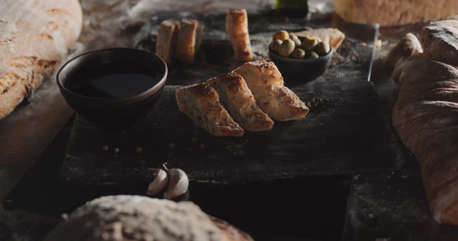 Slices of bread displayed on wood tray with olives and balsamic vinegar