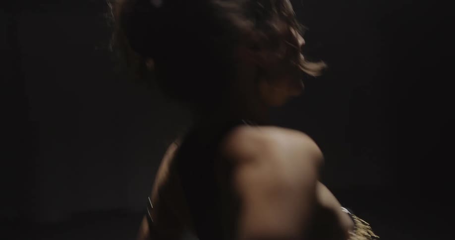 A woman is belly dancing as she moves her arms and body in the darkness