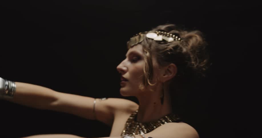 Young woman wearing jewelry performs an exotic dance on a dark room