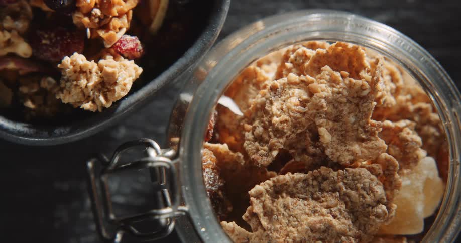 An up close view of granola in a glass jar next to a bowl of granola