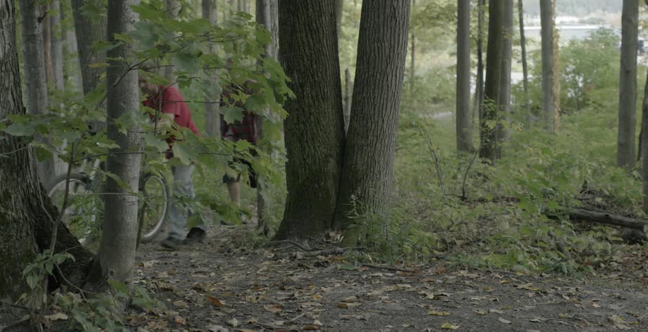 A person pushes a bike in the woods as another follows