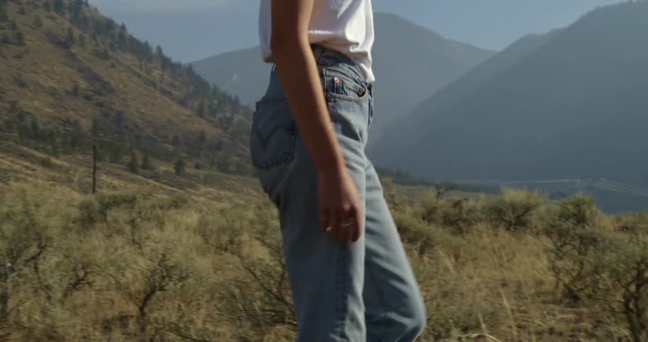 Woman in white t shirt and jeans walks across field in mountainous region
